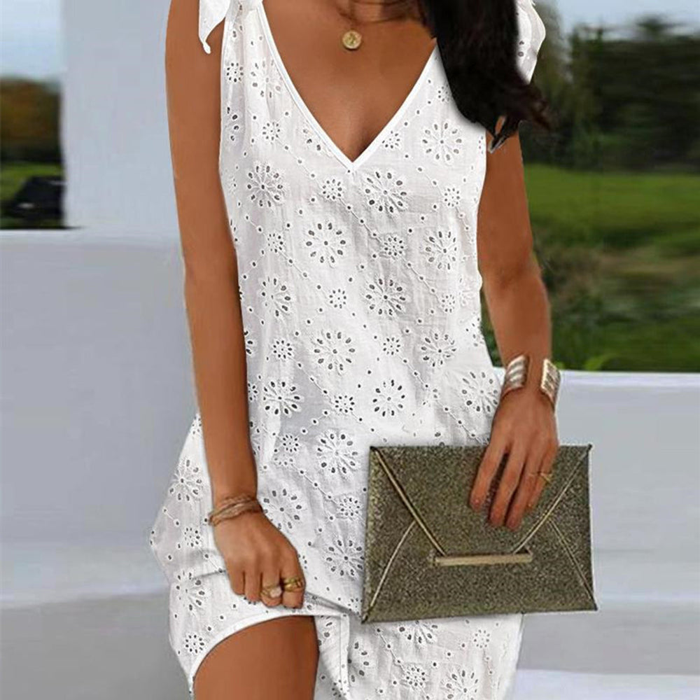 Witte zomerjurk met broderie anglaise patroon, mouwloos en V-hals, gecombineerd met een glinsterende gouden clutch. Perfect voor zomerse evenementen.