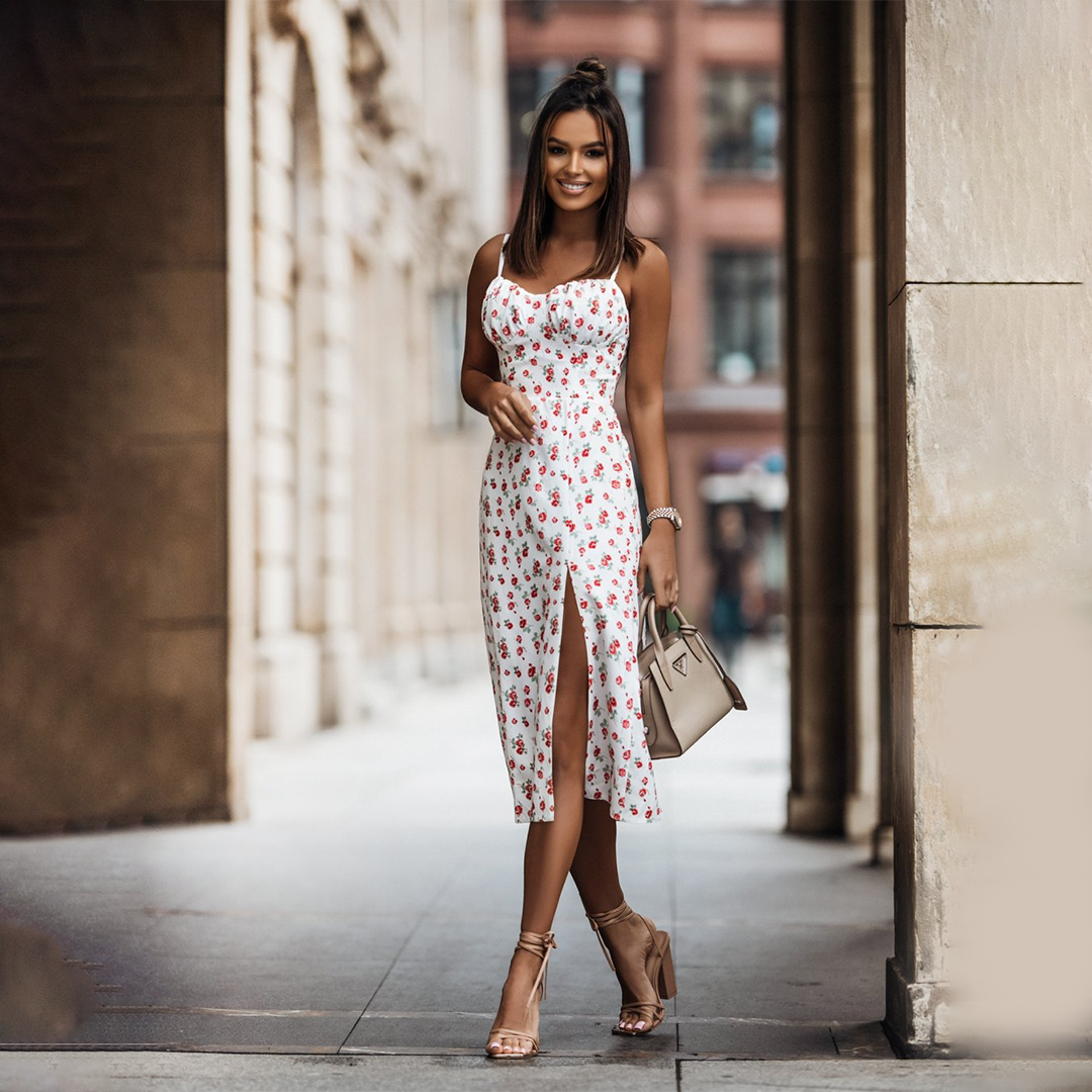Witte zomerjurk met bloemenprint en split, gedragen door vrouw in stedelijke omgeving. Perfect voor casual en elegante zomermode.