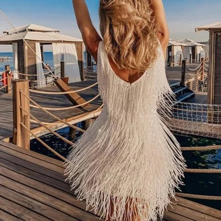 Vrouw in witte franjesjurk op houten pier bij zee, zomerse mode, strandkleding, elegante avondjurk, vakantieoutfit, trendy dameskleding.