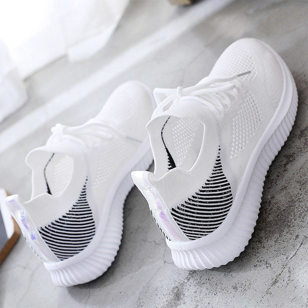 Witte sportschoenen met ademend mesh, zwarte accenten en dikke zool op betonnen vloer. Moderne sneakers voor hardlopen en casual gebruik.