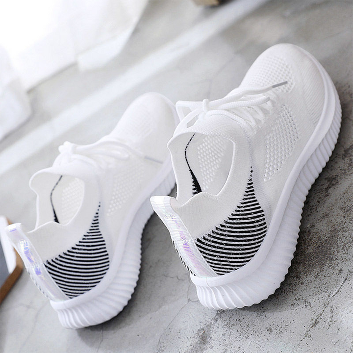 Witte sportschoenen met ademend mesh, zwarte accenten en dikke zool op betonnen vloer. Moderne sneakers voor hardlopen en casual gebruik.