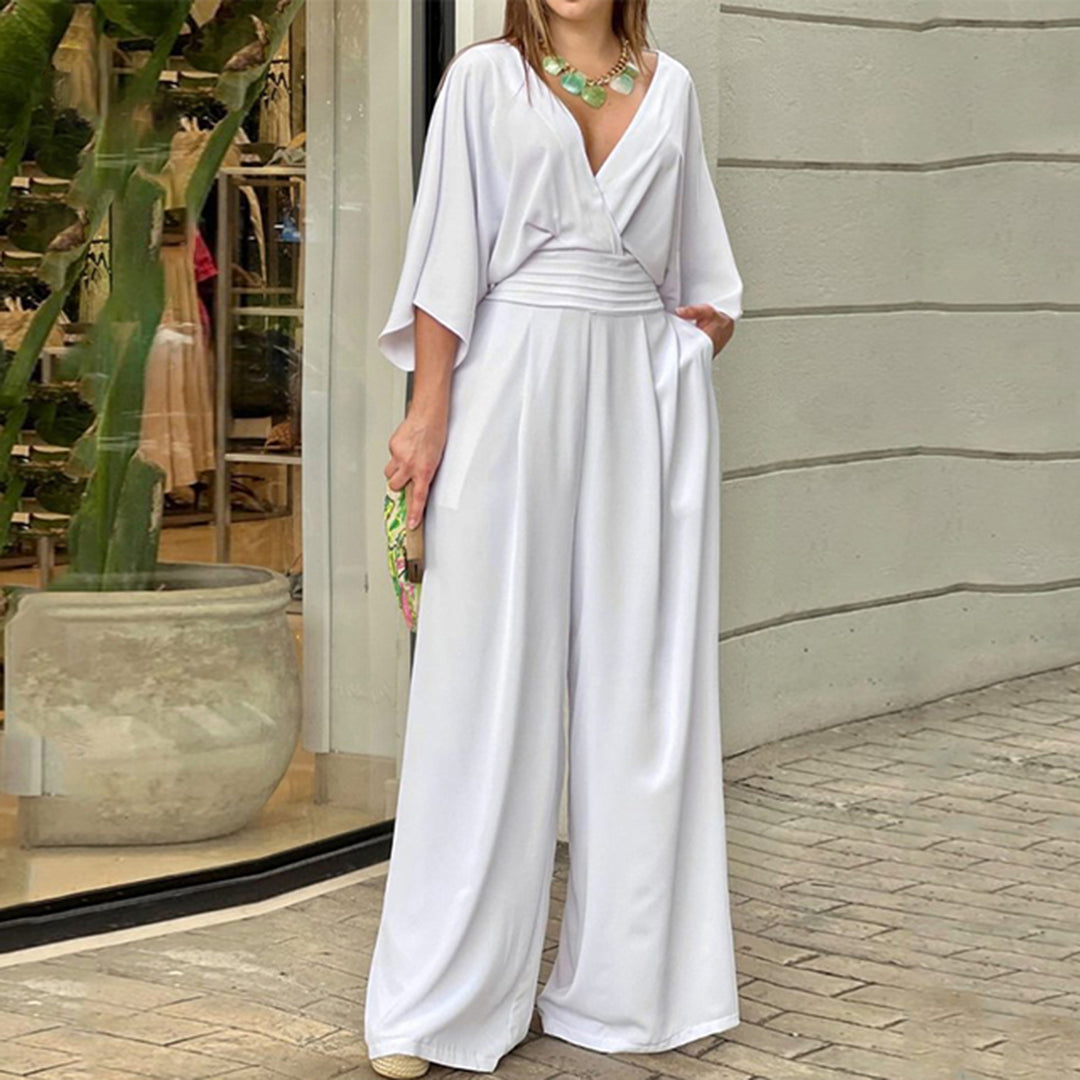 Vrouw in elegante witte jumpsuit met wijde pijpen, V-hals en korte mouwen, poseert buiten bij winkel. Trendy damesmode, zomeroutfit.