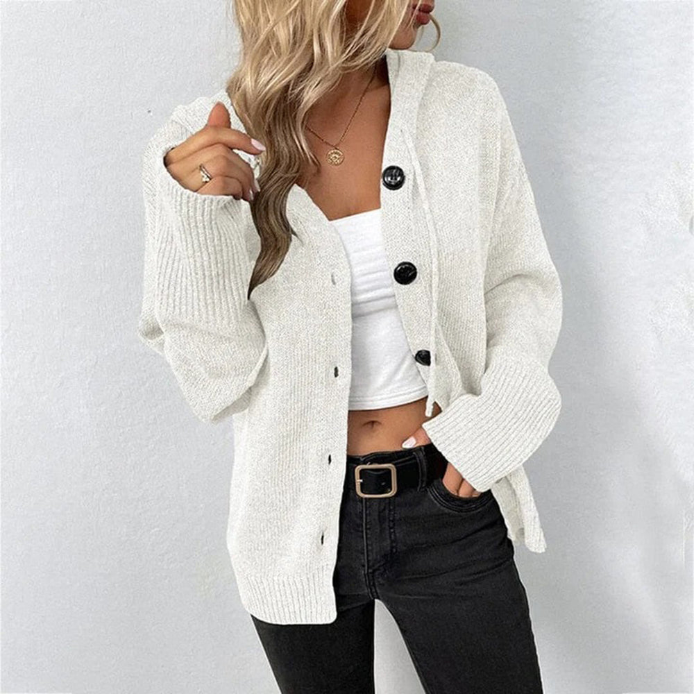 Vrouw draagt witte gebreide cardigan met zwarte knopen, gecombineerd met een wit topje en zwarte jeans. Modieuze dameskleding, casual stijl.