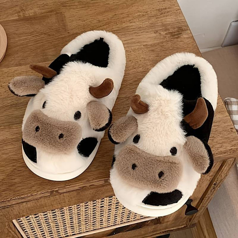 Pluche pantoffels in koeienmotief met bruine hoorns en oren, zwart-witte vlekken, op houten kast. Comfortabele, warme sloffen voor thuis.