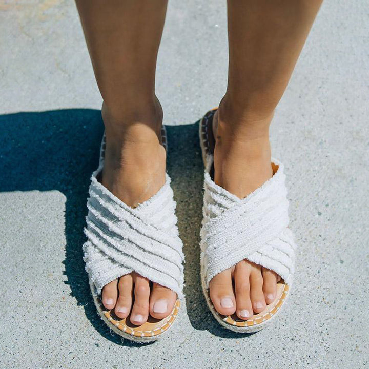 Witte sandalen met gekruiste bandjes op blote voeten, zomerschoeisel voor dames, comfortabele en stijlvolle espadrilles op een betonnen ondergrond.