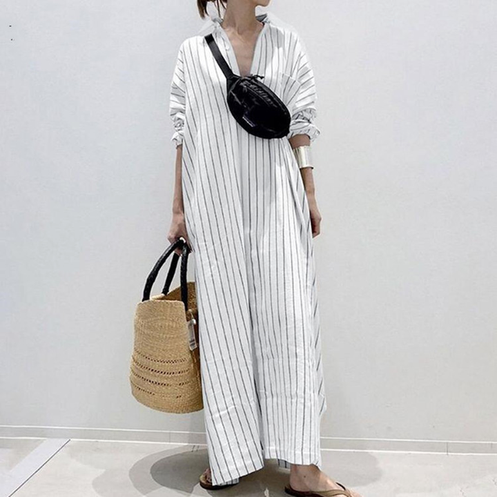 Vrouw in lange, wit gestreepte jurk met zwarte heuptas en rieten tas. Modieuze zomeroutfit, casual stijl, comfortabele dameskleding.