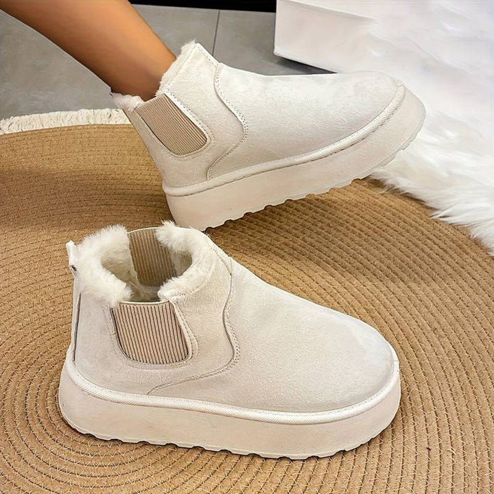 Witte dames enkellaarsjes met bontvoering, elastische inzetstukken en dikke zool op een ronde mat. Trendy wintermode, comfortabele schoenen.