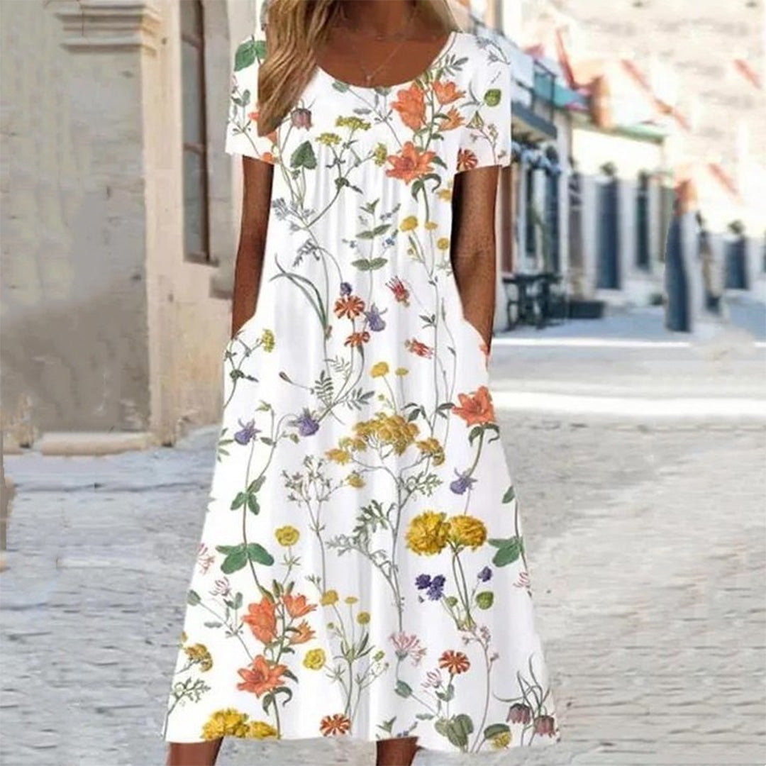 Vrouw in witte zomerjurk met kleurrijke bloemenprint, staand op een zonnige straat. Perfecte casual outfit voor warme dagen.