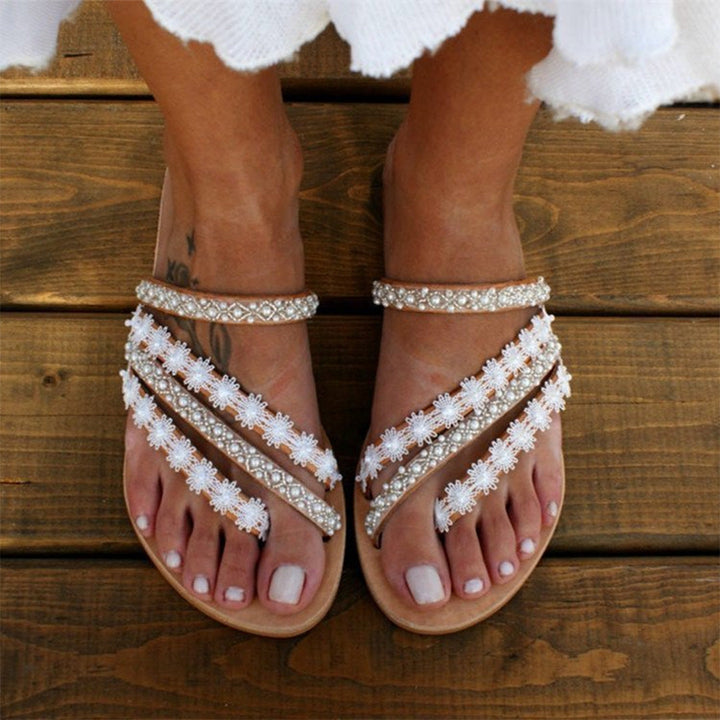 Witte sandalen met bloemenpatroon en parels op houten vloer. Zomerschoenen, damesmode, boho-stijl, strandaccessoires.