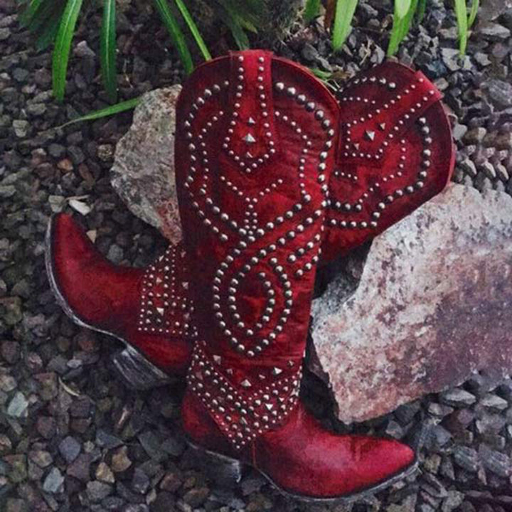 Rode cowboylaarzen met zilveren studs op grind en stenen, westernstijl, leren laarzen, opvallend design, outdoor modeaccessoire.