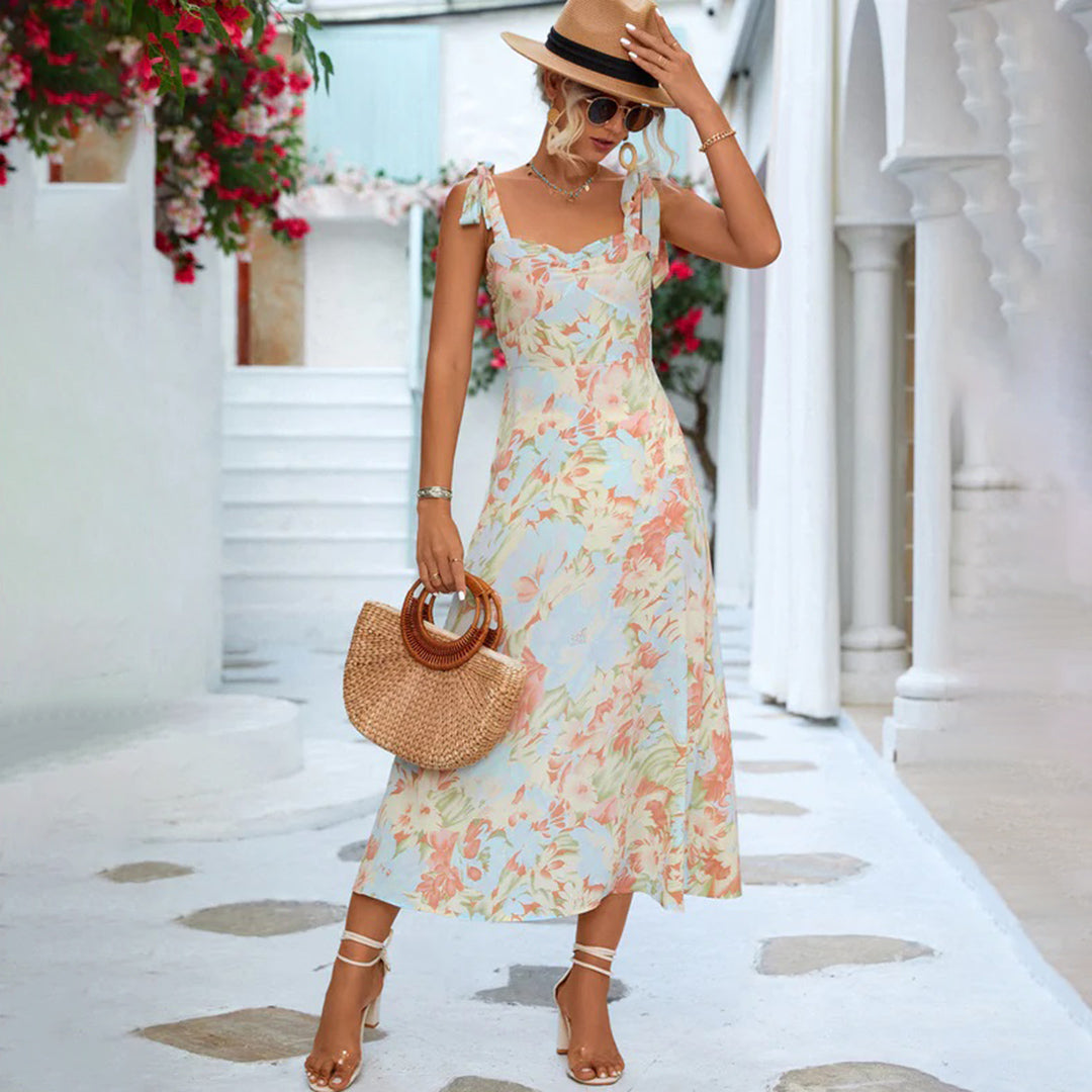 Vrouw in zomerse bloemenjurk met strohoed en rieten tas, poseert in mediterrane straat. Perfecte outfit voor zomermode en vakantie.