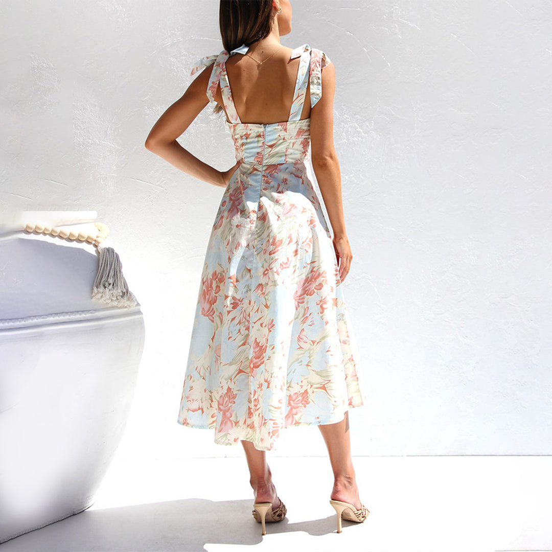 Vrouw in elegante, bloemenjurk met open rug, staand tegen witte achtergrond. Zomermode, dameskleding, stijlvolle jurk, pastelkleurig design.