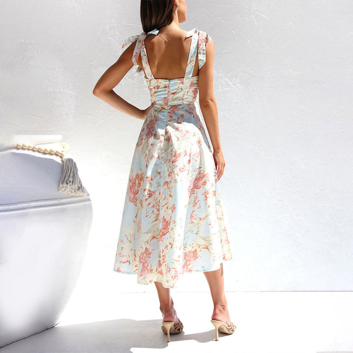 Vrouw in elegante, bloemenjurk met open rug, staand tegen witte achtergrond. Zomermode, dameskleding, stijlvolle jurk, pastelkleurig design.