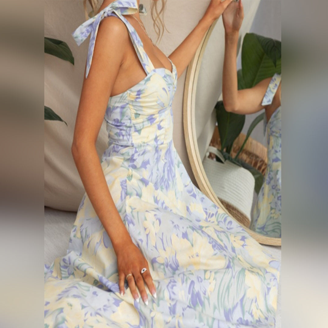 Vrouw in blauwe bloemenjurk met strikbandjes, zittend voor spiegel. Zomerse mode, elegante dameskleding, trendy jurk, casual chique stijl.