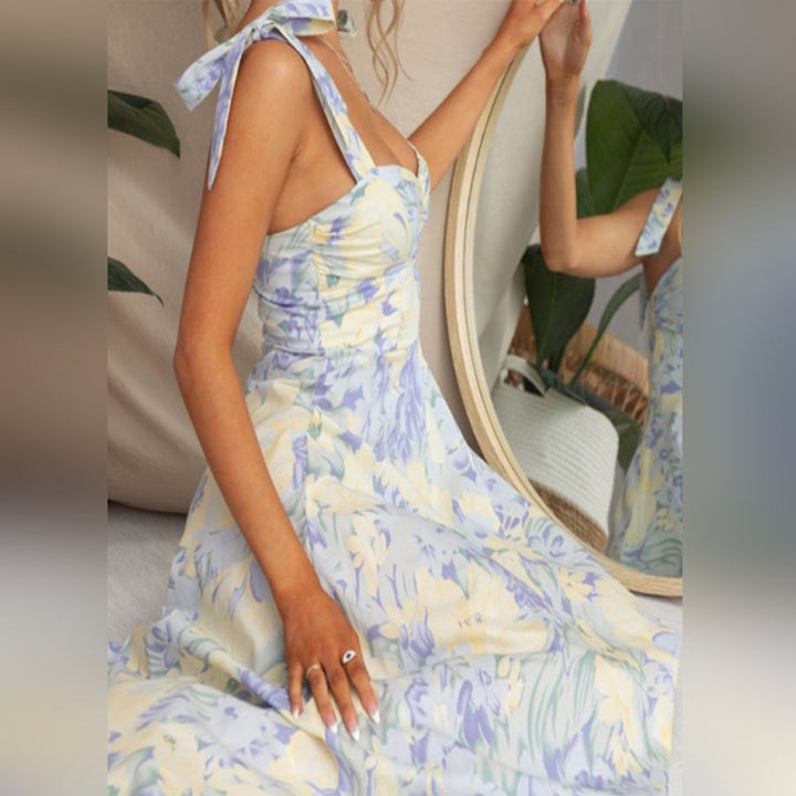 Vrouw in blauwe bloemenjurk met strikbandjes, zittend voor spiegel. Zomerse mode, elegante dameskleding, trendy jurk, casual chique stijl.