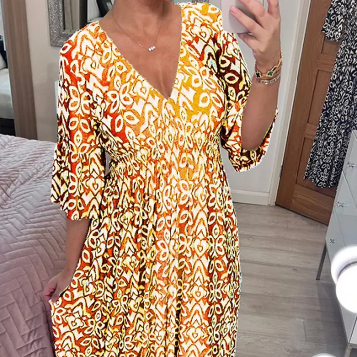 Vrouw in spiegel selfie met gele bohemian jurk met bloemenprint, diepe V-hals en wijde mouwen. Trendy zomerjurk voor casual en feestelijke gelegenheden.
