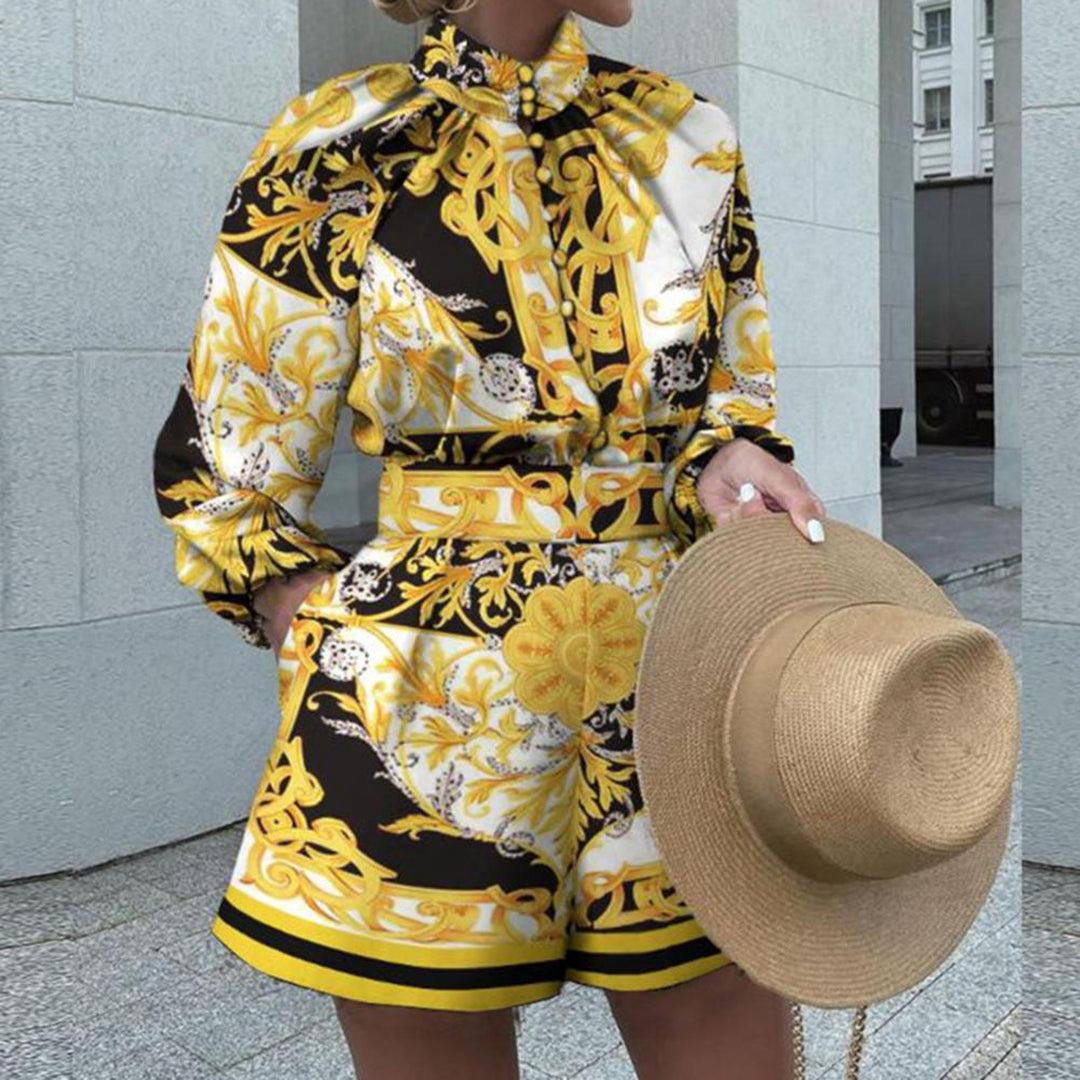 Vrouw in stijlvolle gele en zwarte barokprint jumpsuit met lange mouwen, houdt een strohoed vast. Perfect voor zomermode en elegante outfits.