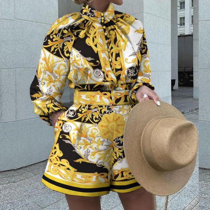 Vrouw in stijlvolle gele en zwarte barokprint jumpsuit met lange mouwen, houdt een strohoed vast. Perfect voor zomermode en elegante outfits.