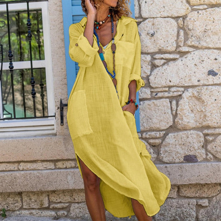 Vrouw in gele linnen jurk met lange mouwen, casual stijl, voor stenen muur. Zomermode, comfortabele dameskleding, boho accessoires.